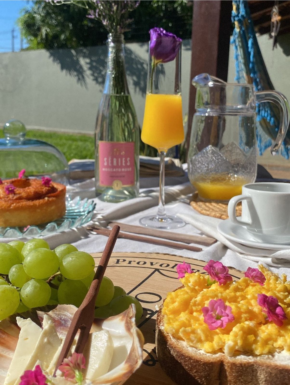Mesa de café da manhã com frutas, ovos mexidos, suco e espumante rosa no jardim